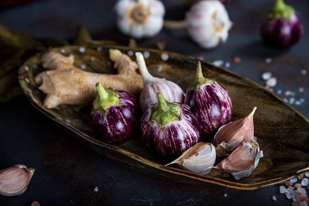 Mini aubergines, gingembre, ail dans une assiette en céramique faite à la main, sel rose cristallin sur béton