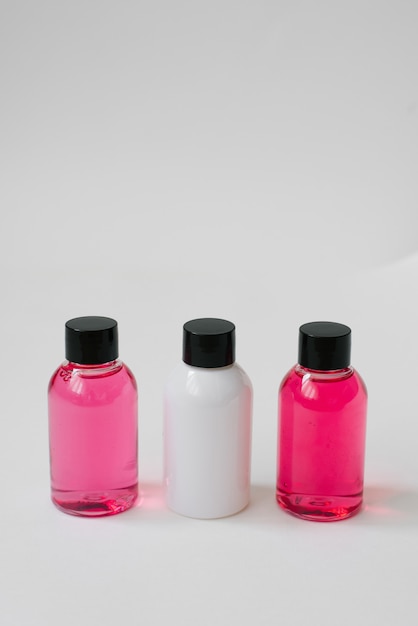 Mini bouteilles de couleur rose et blanche avec des cosmétiques ou des cheveux sur fond blanc