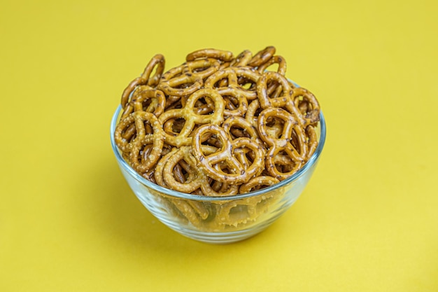 Mini bretzels salés dans un bol en verre profond sur fond jaune. Snack à la bière populaire. Espace pour le texte.