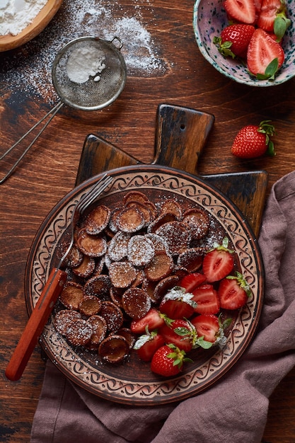 Mini céréales de crêpes au chocolat avec des fraises pour le petit déjeuner sur la vieille table en bois. Petit-déjeuner maison branché avec de minuscules crêpes. Vue de dessus.