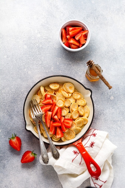 Mini céréales crêpes blanches aux fraises dans une poêle pour le petit déjeuner sur une surface grise. Vue de dessus.