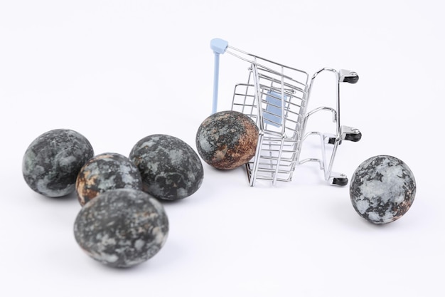 Mini chariot de supermarché avec des oeufs de Pâques peints en marbre gris sur fond blanc