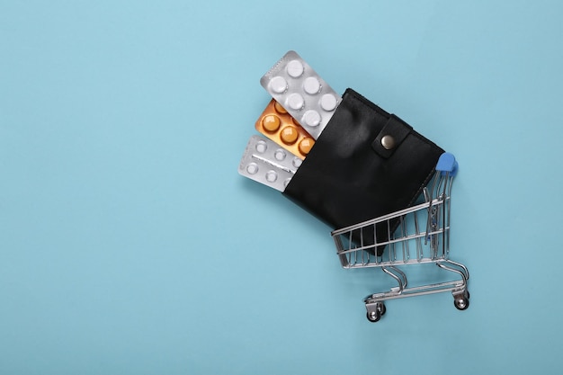 Mini chariot de supermarché et sac à main avec blister de pilules sur fond bleu