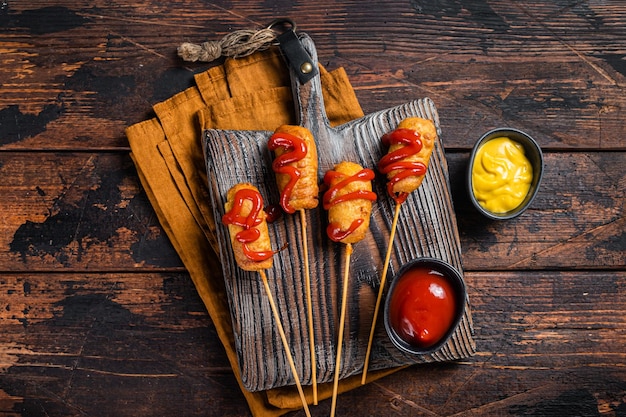 Mini chiens de maïs frits avec de la moutarde et du ketchup sur une planche en bois Fond en bois Vue de dessus