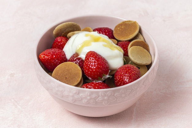 Mini crêpe de céréales maison avec du yaourt, du miel et des fraises sur une table colorée.