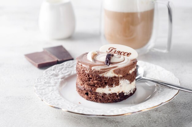 Mini gâteau au chocolat dans une élégante assiette blanche et cappuccino avec mousse dans une tasse en verre sur fond gris clair, vue de dessus. Dessert délicieux. Couverts de table de petit-déjeuner.