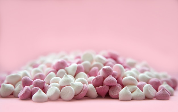 Mini meringues roses et blanches en forme de gouttes, qui reposent sur une surface rose.