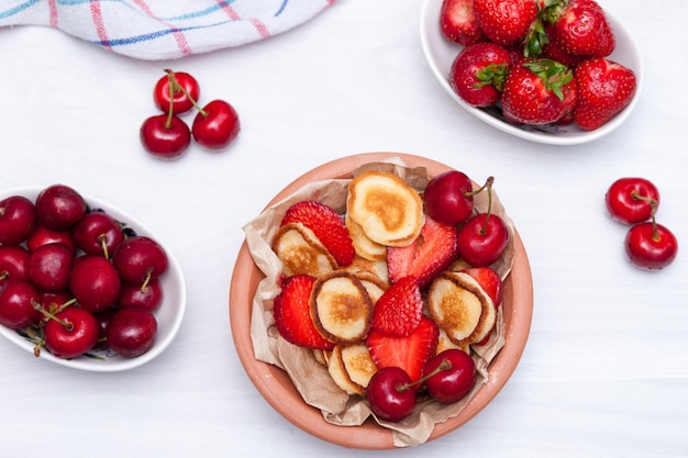 Mini minuscules crêpes aux fraises et cerises sur fond de bois blanc. Concept de cuisine à la mode. Mise à plat.