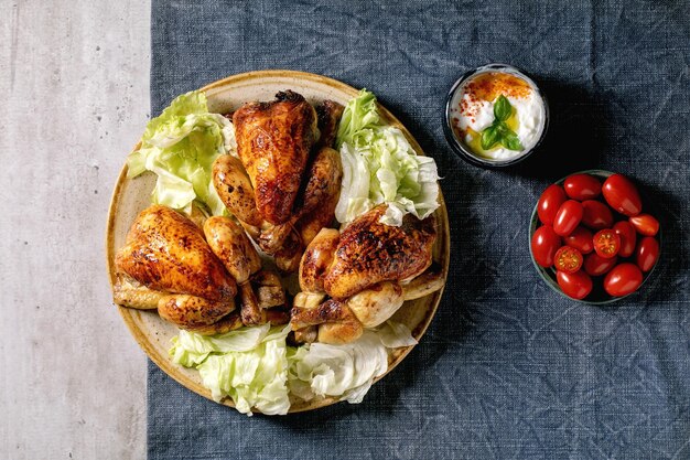 Mini poulet entier rôti avec salade verte sur assiette en céramique, sauce au yaourt, tomates cerises sur nappe en lin bleu. Mise à plat, espace de copie