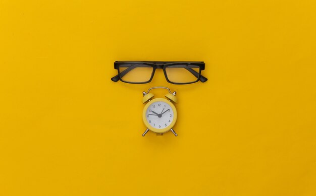 Mini réveil et lunettes sur fond jaune.