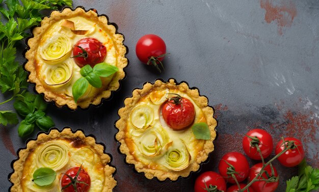 Mini tarte aux poireaux au four, tomates cerises et sauce crème sur fond de béton gris. Mise au point sélective. Style rustique. Vue de dessus.