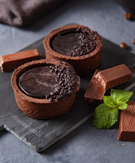 Mini tartelettes au chocolat avec morceau de chocolat sur fond sombre. Image de la vue macro
