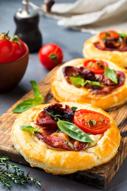 Mini tartelettes à la viande séchée, tomates, ricotta, thym, basilic et olives sur un béton gris. Style rustique