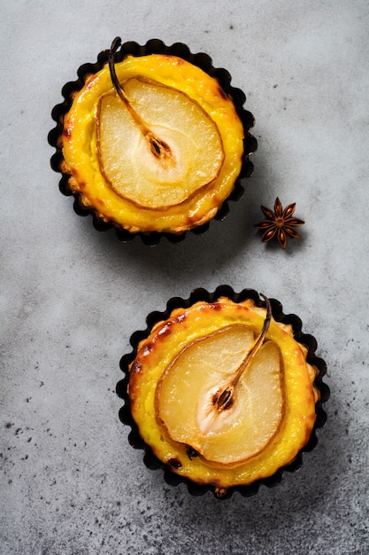 Mini-tartes aux poires et crème anglaise sur un vieux fond de table en béton gris foncé