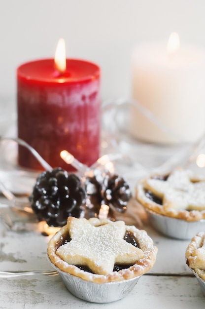 Mini tartes hachées servies avec bougie rouge et blanche, pommes de pin et lumières décoratives