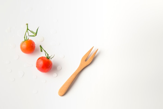 Mini-tomates fraîches avec une fourchette en bois sur fond blanc