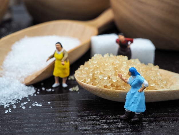 Miniature femme grosse debout près d&#39;un bol en bois et une cuillère avec un morceau de sucre sur backg bois foncé