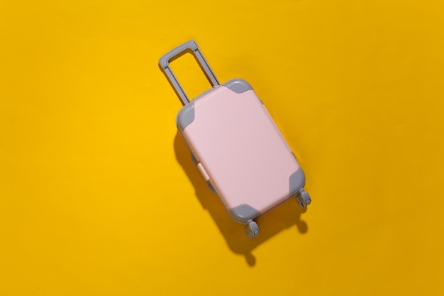 Minimalisme de voyage. Mini valise de voyage en plastique sur fond jaune avec ombre profonde. Style minimaliste. Vue de dessus, mise à plat