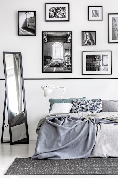 Photo miroir à côté du lit avec des draps gris à l'intérieur de la chambre minimale blanche avec des affiches photo réelle