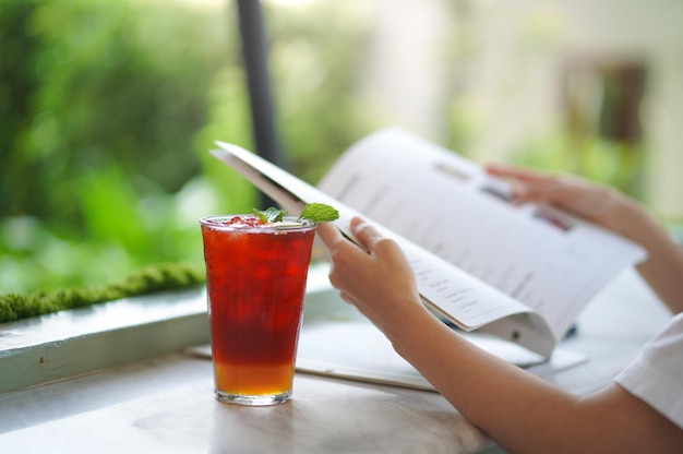 Mise au point douce et mise au point sélective verre de thé au citron et au miel glacé sur table avec livre de tenue de main floue.