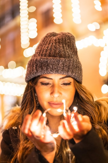 Mise au point peu profonde d'une femme portant un bonnet et posant tout en tenant des lumières de Noël à l'extérieur
