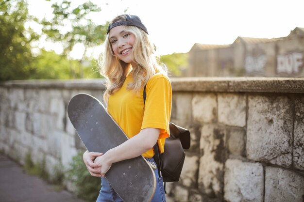 Mise au point peu profonde d'une jeune femme blonde souriante avec une planche à roulettes posant dans un pair