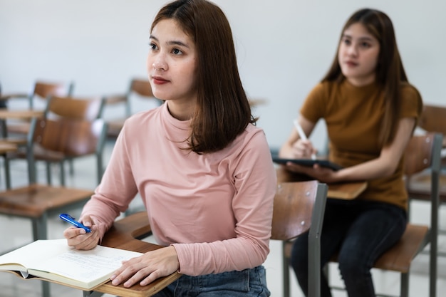 Mise au point sélective des adolescents assis sur une chaise de conférence en classe écrivant sur la feuille de réponses du papier d'examen en effectuant le test d'examen final. Étudiantes dans l'uniforme étudiant.
