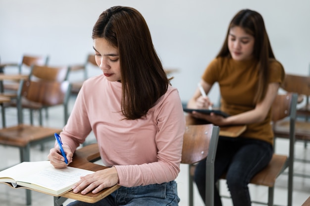 Mise au point sélective des adolescents assis sur une chaise de conférence en classe écrivant sur la feuille de réponses du papier d'examen en effectuant le test d'examen final. Étudiantes dans l'uniforme étudiant.