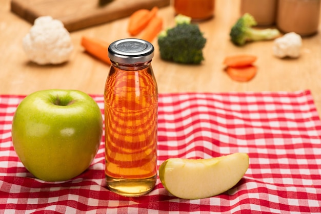 Mise au point sélective d'une bouteille de jus de pomme et d'aliments pour bébés dans des bocaux avec des ingrédients sur la nappe