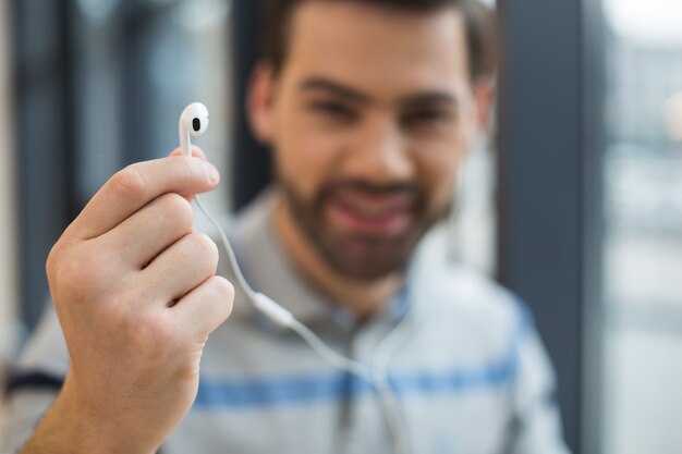 Mise au point sélective d'un casque étant dans une main d'un bel homme joyeux positif tout en écoutant de la musique