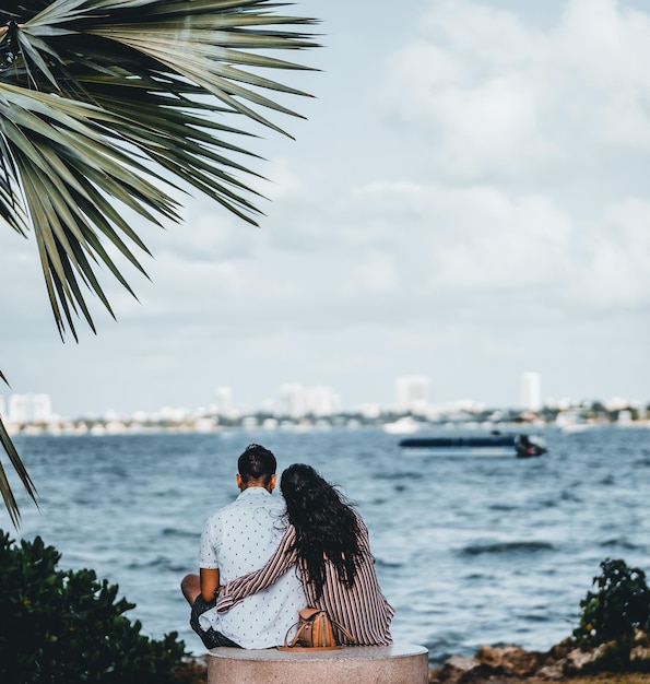 Mise au point sélective d'un couple d'amoureux par derrière se serrant les coudes et regardant la mer