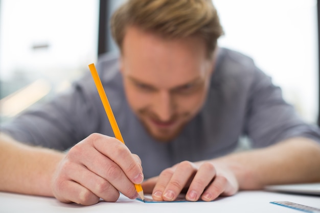 Mise au point sélective d'un crayon jaune utilisé par un homme ravi joyeux tout en faisant un dessin professionnel