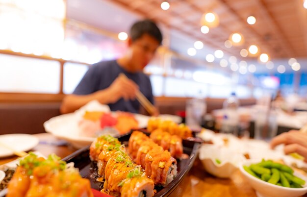 Mise au point sélective sur la cuisine japonaise dans un restaurant japonais. Sushi au saumon sur une assiette avec un homme flou mangeant de la nourriture japonaise avec des baguettes dans le restaurant. Cuisine asiatique saine. Menu de sushis au saumon.