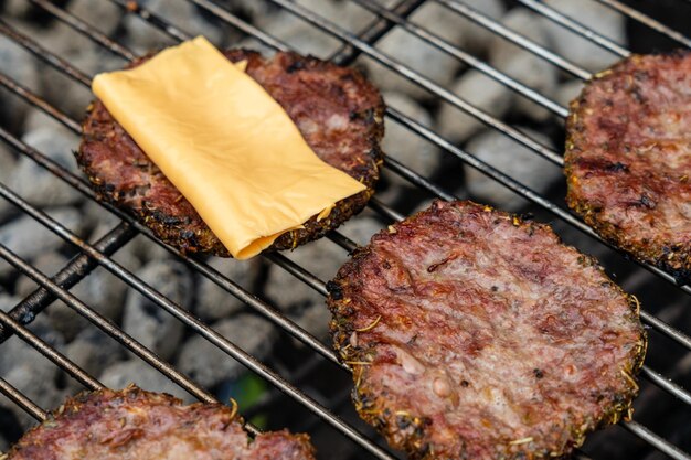 Mise au point sélective de délicieuses escalopes de burger fraîches avec grillades de fromage sur le gril du barbecue