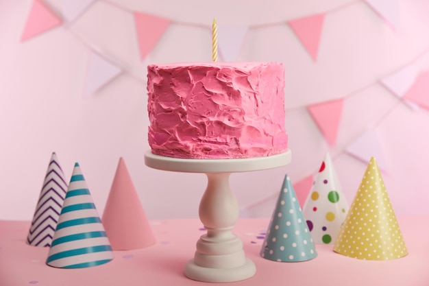 Mise au point sélective d'un délicieux gâteau d'anniversaire rose avec une bougie sur un présentoir à gâteaux près des casquettes de fête et de la décoration