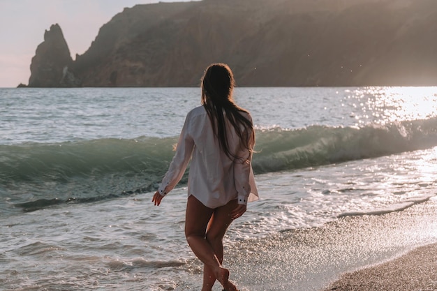 Mise au point sélective heureuse femme sensuelle insouciante aux cheveux longs en maillot de bain noir posant sur la plage au coucher du soleil