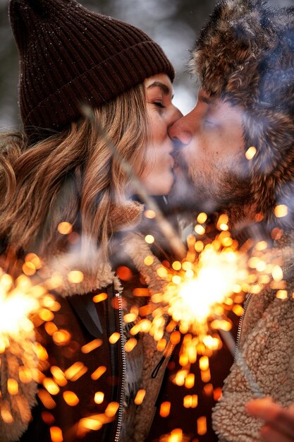 Photo mise au point sélective histoire d'amour de couple dans la forêt enneigée s'embrasser et tenir un couple de cierges magiques en hiver nature couple célébrant la date de la saint-valentin