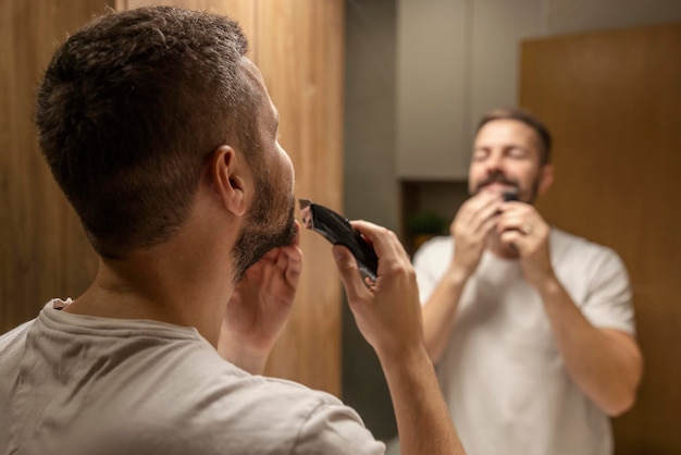 Mise au point sélective sur l'homme se rasant la barbe en se tenant debout dans la salle de bain