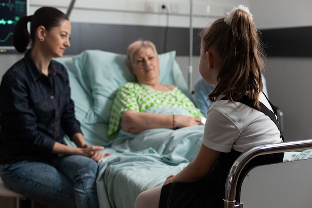 Photo mise au point sélective sur une jeune grand-mère rendant visite à une grand-mère à la retraite malade dans une salle d'hôpital