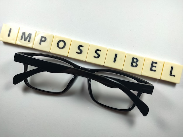 Mise au point sélective Lettres de Scrabble avec texte IMPOSSIBLE et lunettes sur fond blanc