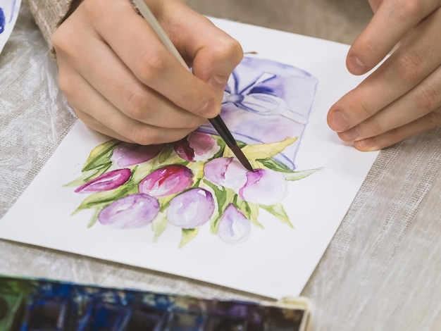 Photo mise au point sélective main d'artiste avec peinture au pinceau sur toile pinceau entre les mains de l'artiste peinture à l'aquarelle créativité avec de nombreuses couleurs