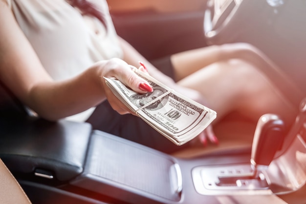 Mise au point sélective sur la main féminine avec un paquet de dollars à l'intérieur de la voiture