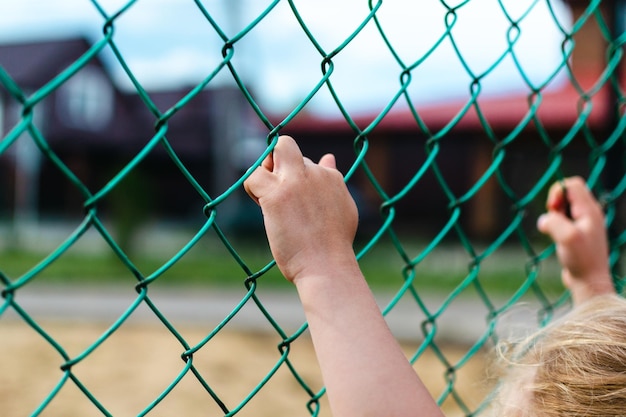 Mise au point sélective sur la main d'un petit enfant saisissant une clôture en treillis métallique, espace de copie.