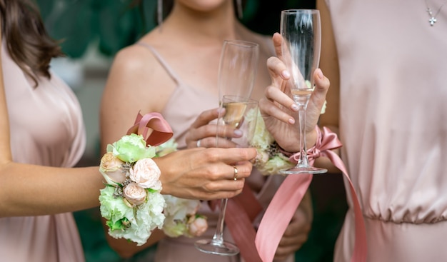 mise au point sélective sur les mains des demoiselles d'honneur en robes de soie rose décorées de fleurs naturelles et de verres de champagne