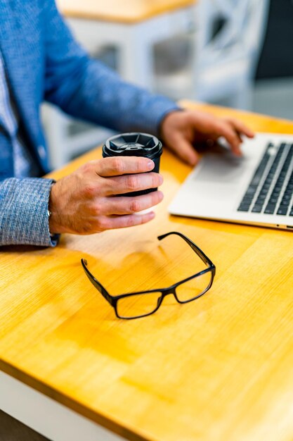 Mise au point sélective sur les mains d'un homme tapant sur un clavier d'ordinateur portable Lunettes modernes dans un cadre noir sur une table Gros plan