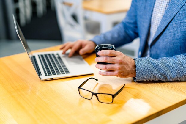 Mise au point sélective sur les mains d'un homme tapant sur un clavier d'ordinateur portable. Verres modernes dans un cadre noir sur une table. Fermer.