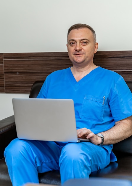 Mise au point sélective sur le médecin en gommages bleus. Assis sur un canapé avec un ordinateur portable.