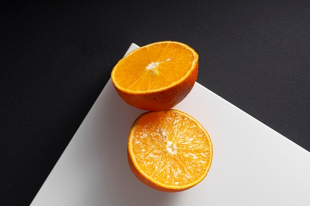 Mise au point sélective, moitiés d'orange juteuse sur un coin carré blanc, sur fond de papier noir