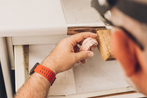 Mise au point sélective sur un moule dentaire entre les mains d'un professionnel moulant les pièces à la cire dans un laboratoire dentaire spécialisé dans la céramique osseuse dentaire pour créer des couronnes en porcelaine