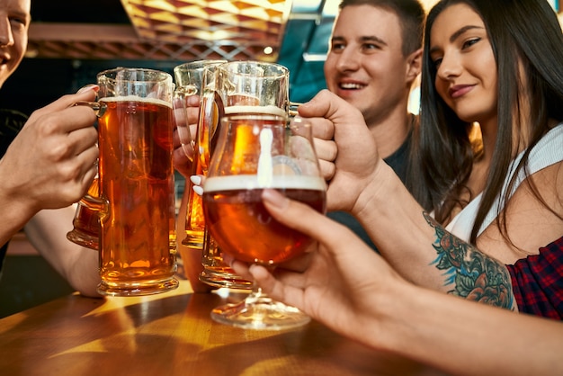 Mise au point sélective de pintes de bière dans les mains de jeunes amis heureux au pub